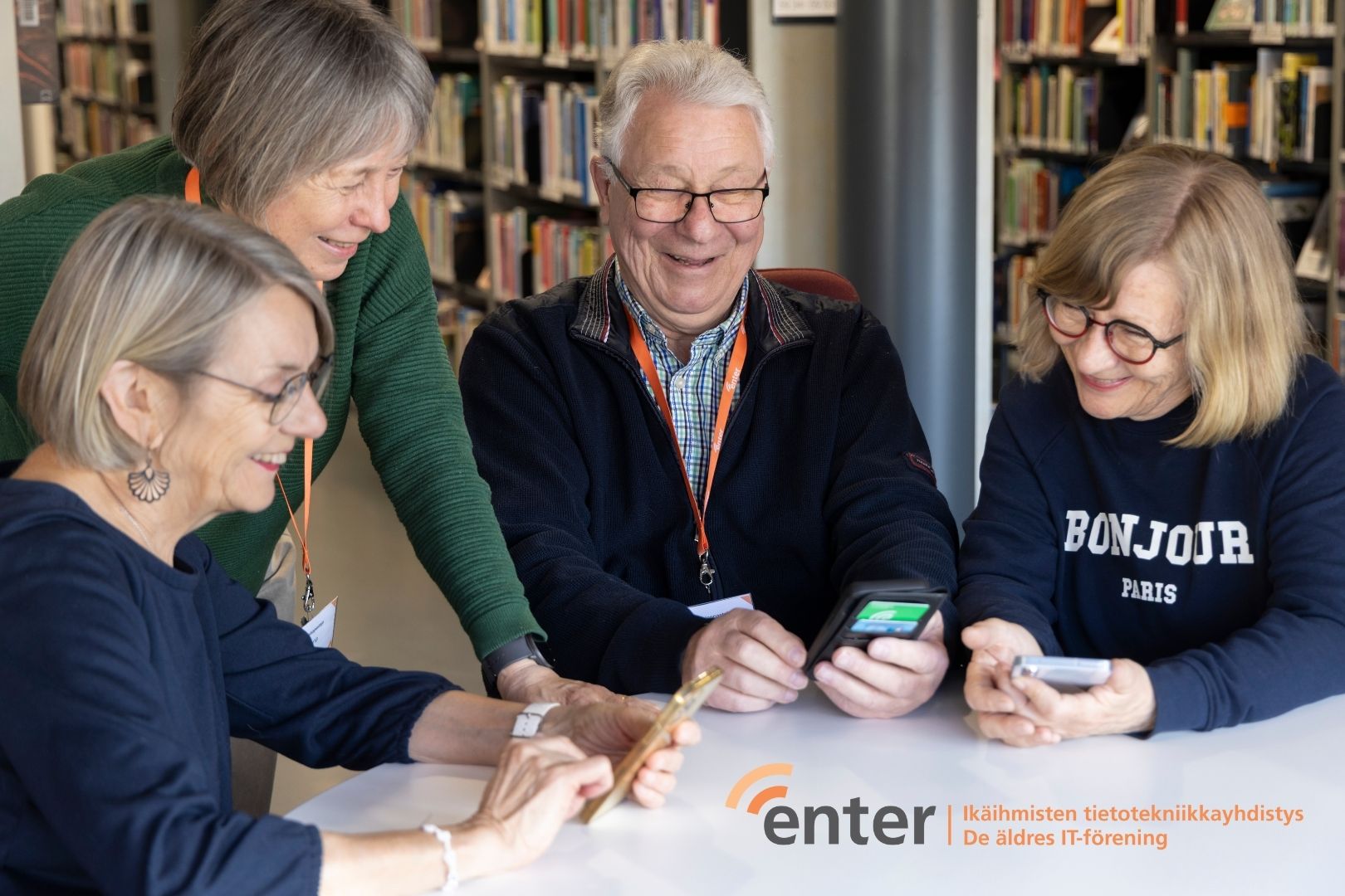 Seniorit käyttävät digilaitteita pöydän ääressä.